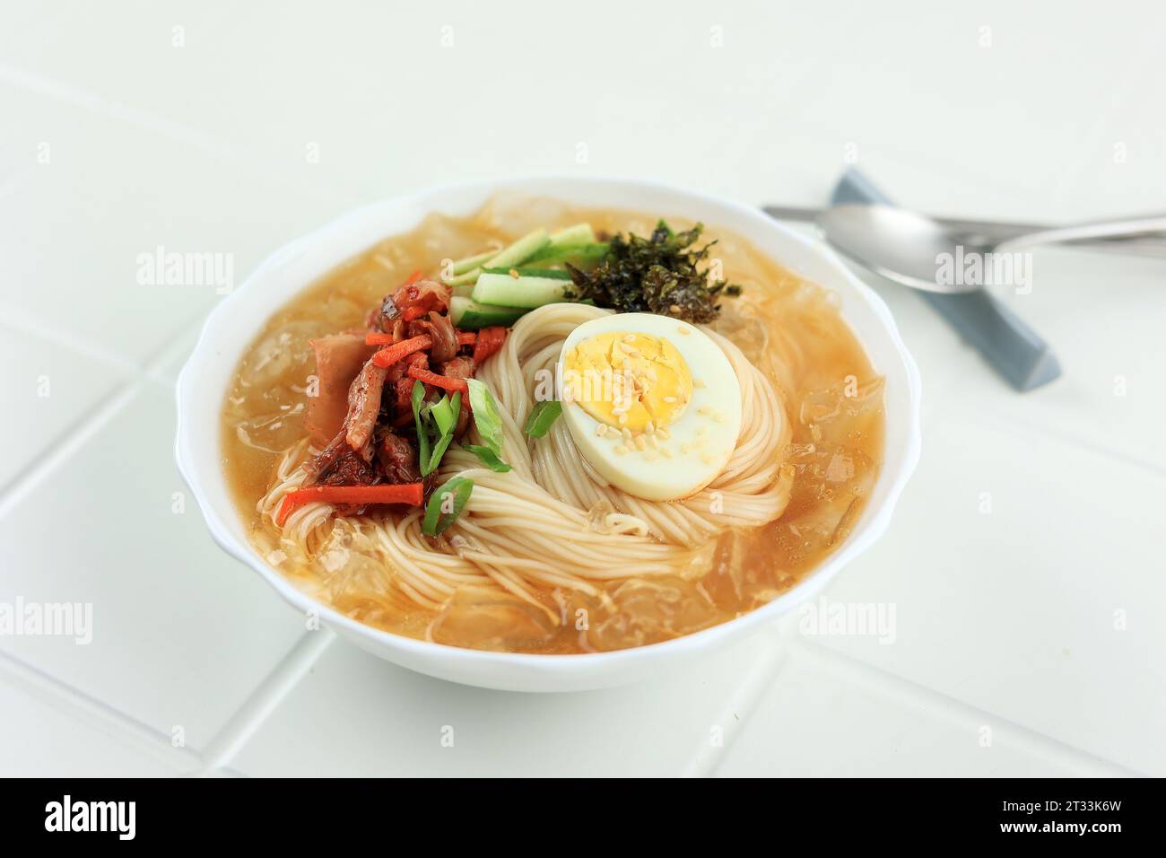 Soupe de nouilles froides coréennes Bibim Guksu servie avec kimchi, glace de roche, flocons de Nori et œuf bouilli Banque D'Images