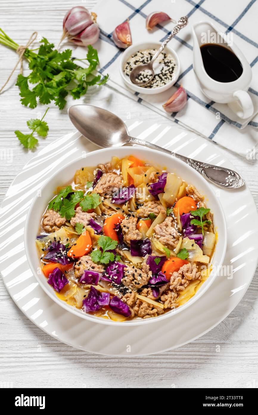 soupe au chou roulé aux œufs avec du porc haché et des légumes dans un bol blanc sur une table en bois blanc avec des ingrédients, cuisine asiatique, vue verticale Banque D'Images
