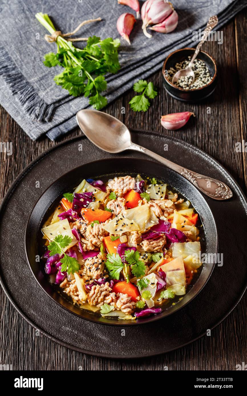 soupe au chou roulé aux œufs avec du porc haché et des légumes dans un bol noir sur une table en bois sombre avec des ingrédients, cuisine asiatique, vue verticale d'en haut Banque D'Images