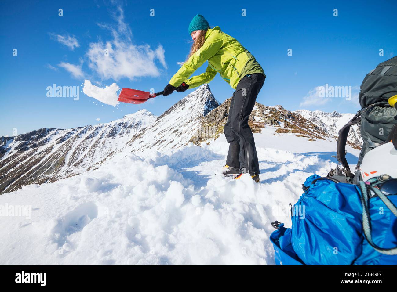 Randonneur féminin pelletant la neige pour faire de la place pour tente, Moskenesoya, Lofoten, Norvège Banque D'Images