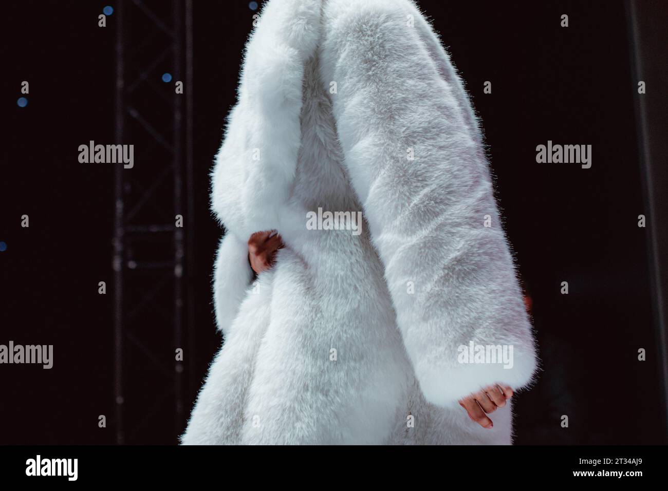 Manteau de fourrure d'hiver blanc moelleux sur un corps féminin. Modèle de mode marchant sur fond noir Banque D'Images