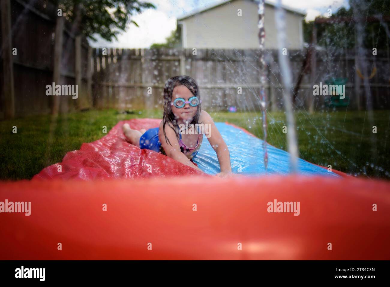 Petite fille jouant sur la glissière d'eau avec des lunettes Banque D'Images