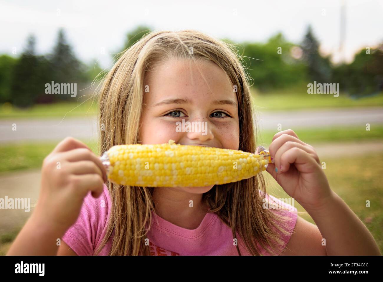 Heureuse jeune fille mangeant du maïs jaune sur l'épi en été Banque D'Images