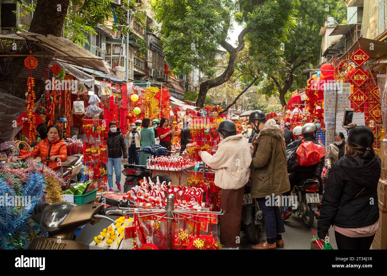 Les Vietnamiens parcourent des stands vendant des cadeaux rouges et dorés colorés pour le Têt, ou nouvel an lunaire, dans une rue bondée de Hang Ma, Hanoi, Vietnam. Banque D'Images