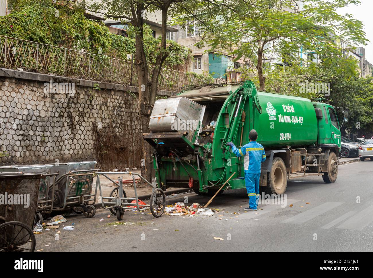Un homme poubelle en uniforme bleu exploite un camion à ordures automatisé à côté des chariots à main traditionnels dans le centre de Hanoi, au Vietnam. Banque D'Images