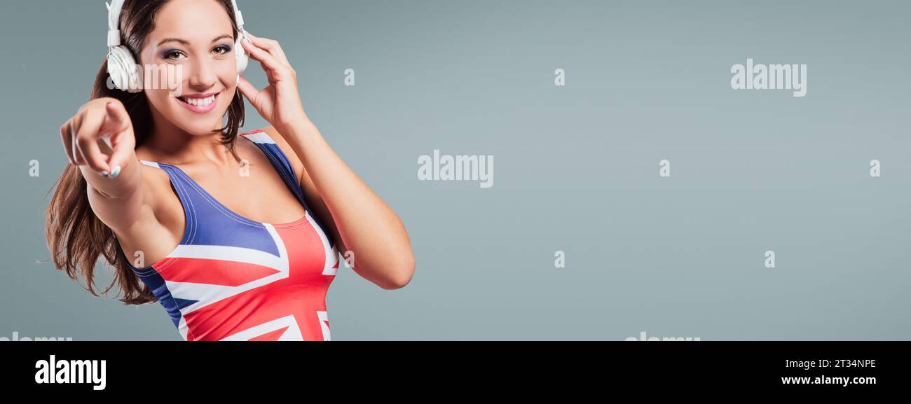 Cheerful pop girl portant un drapeau britannique top, écouter de la musique sur fond blanc Banque D'Images