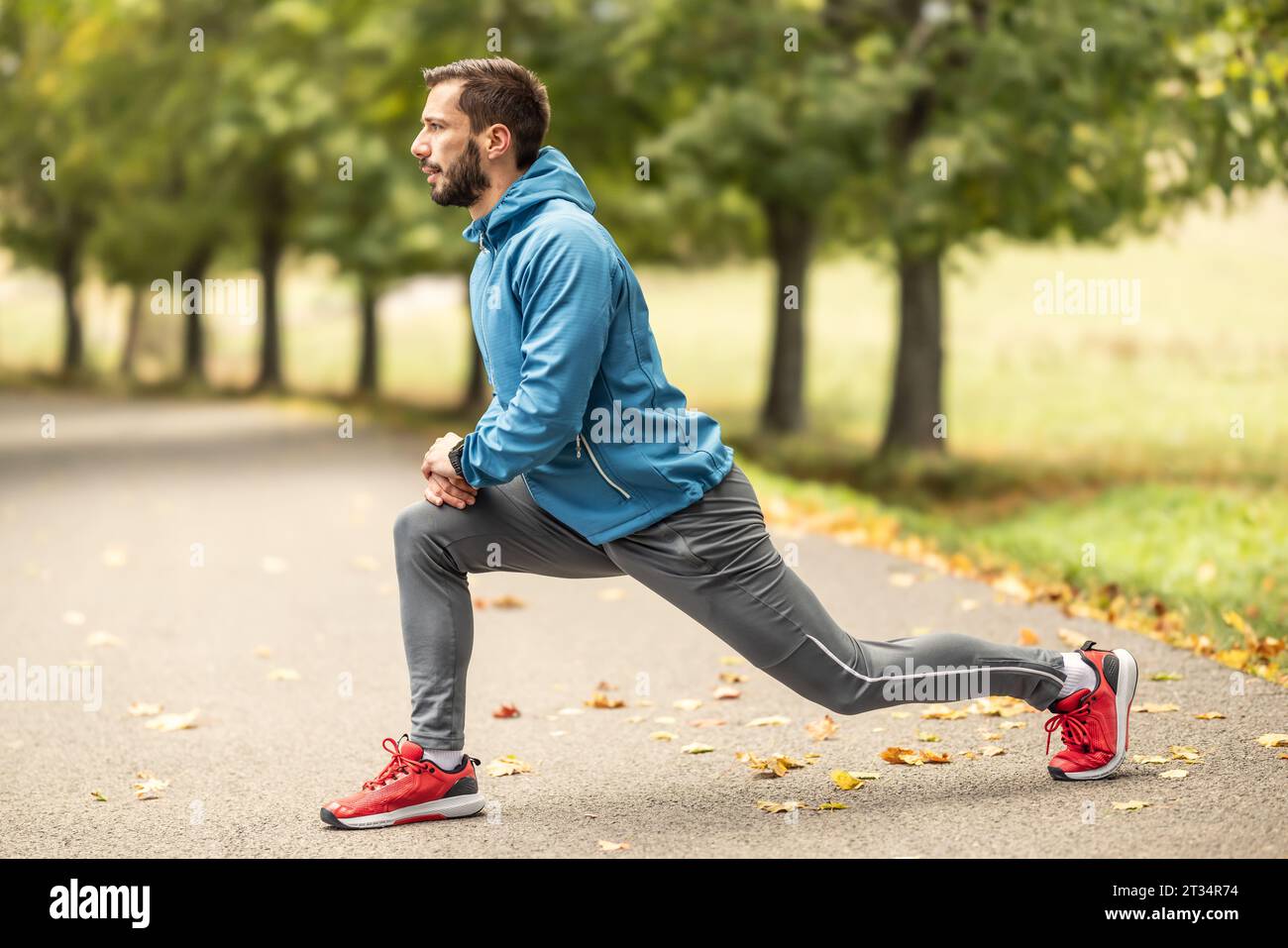 Un jeune athlète s’réchauffe avant de courir s’entraîner dans le parc. Il réchauffe la partie inférieure du corps. Banque D'Images