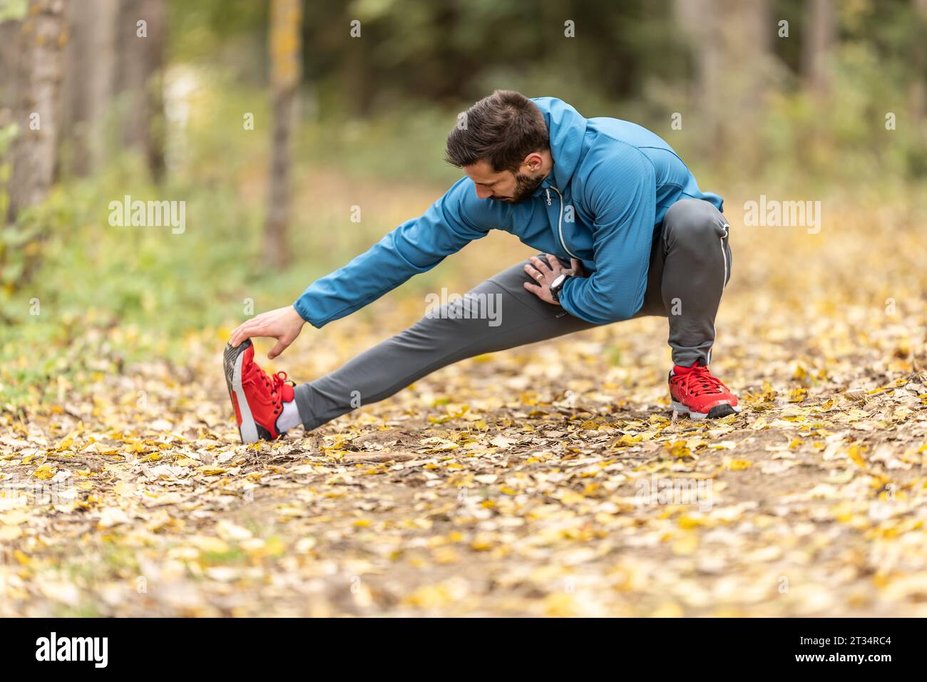 Un jeune athlète s’réchauffe avant de courir s’entraîner dans le parc. Il réchauffe la partie inférieure du corps. Banque D'Images