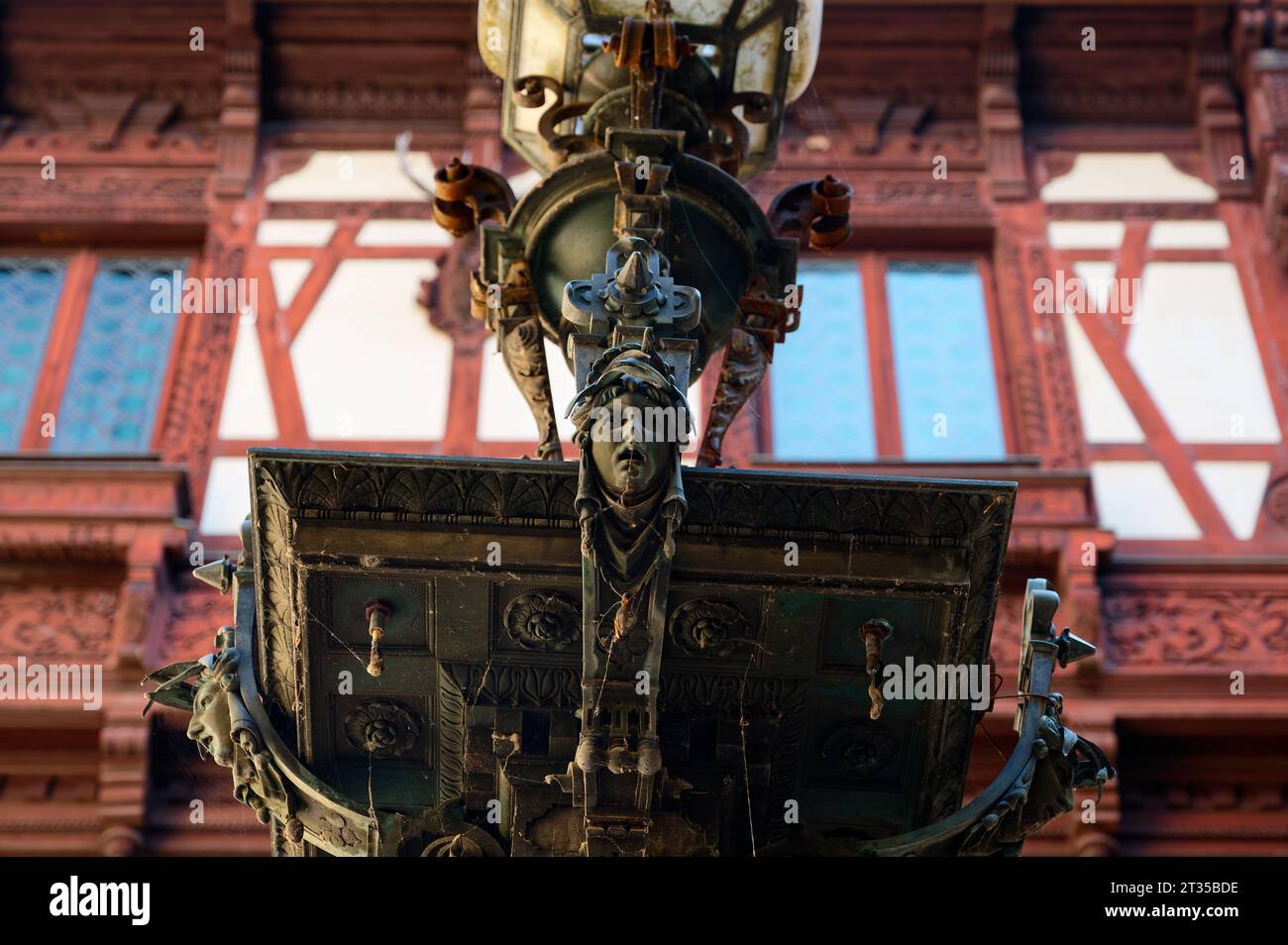 Luminaire orné avec un visage envoûtant dans une charmante cour, avec le magnifique château de Peles offrant une toile de fond colorée. Banque D'Images