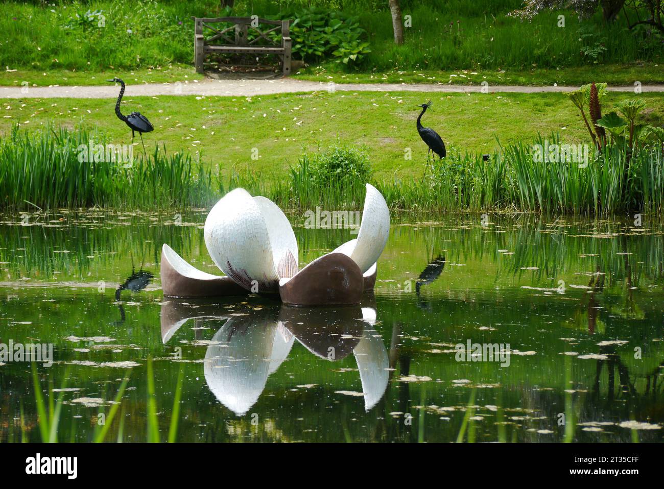 Lys flottant avec Heron & Crane sculptures reflétées dans le lac Magnolia à l'Himalayan Garden & Sculpture Park, North Yorkshire, Angleterre, Royaume-Uni. Banque D'Images