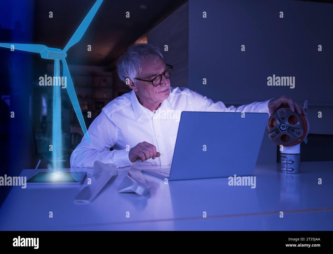 Homme d'affaires avec ordinateur portable examinant la partie de machine au bureau Banque D'Images