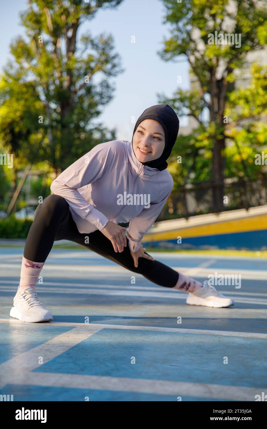 Femme souriante s'étirant sur le terrain de sport Banque D'Images