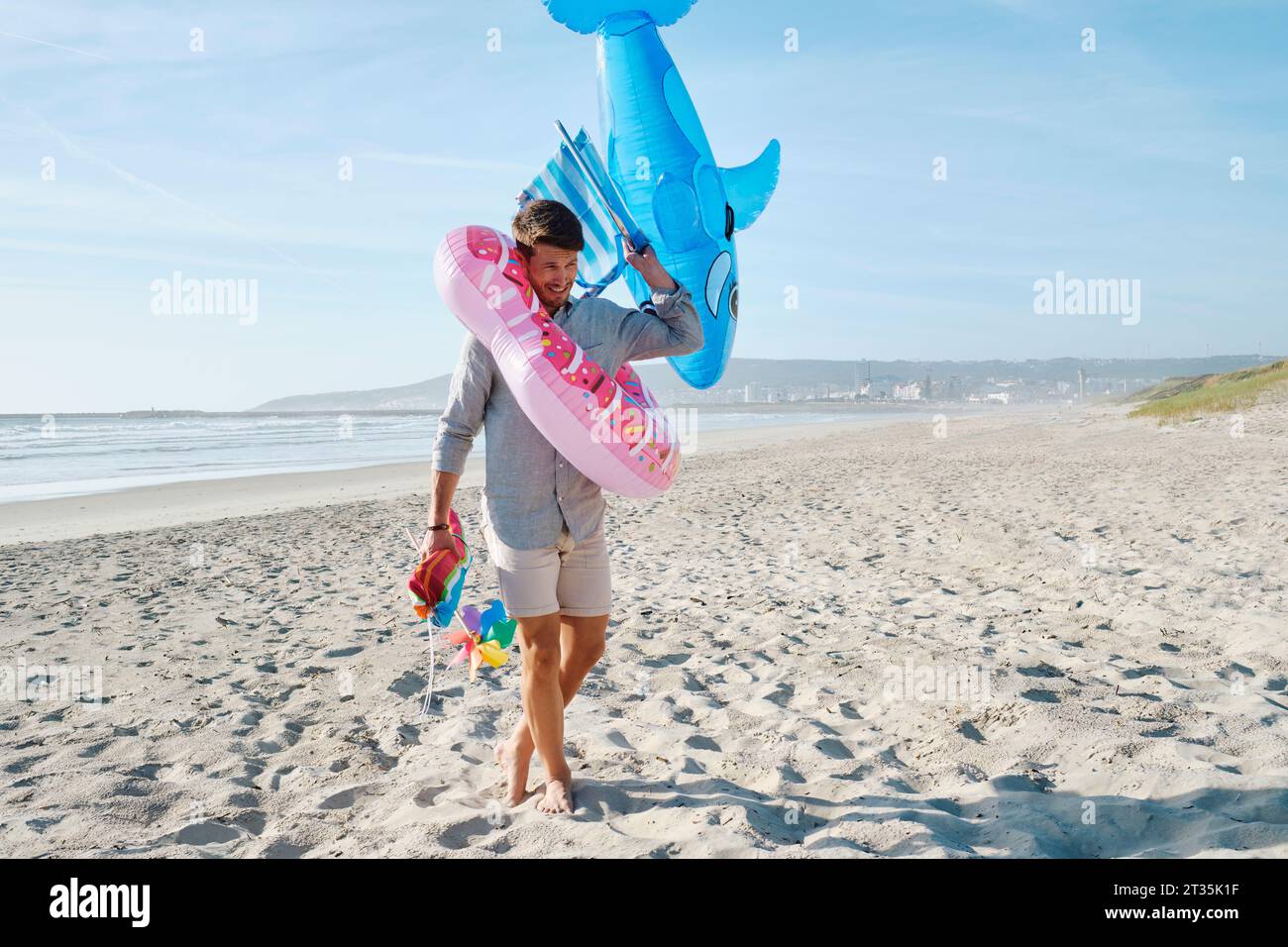 Homme heureux portant anneau de natation gonflable et requin jouet à la plage Banque D'Images