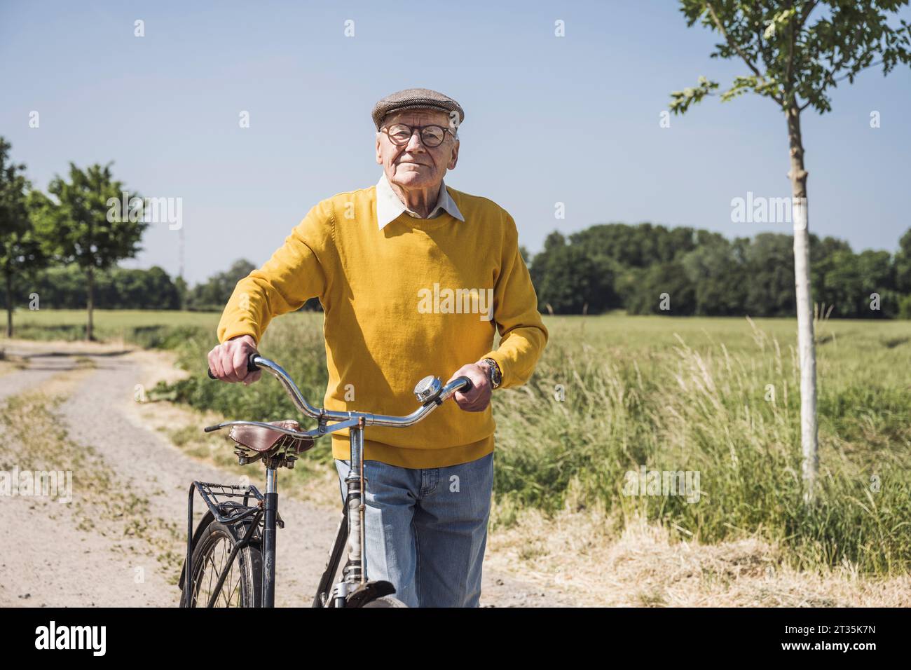 Homme âgé souriant marchant avec le vélo le jour ensoleillé Banque D'Images