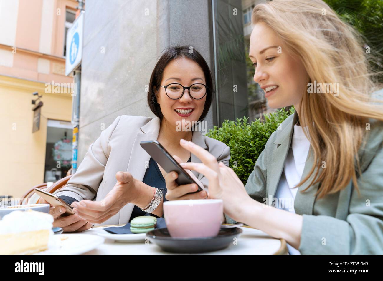 Heureux partenaires d'affaires discutant avec des téléphones intelligents assis au café Sidewalk Banque D'Images
