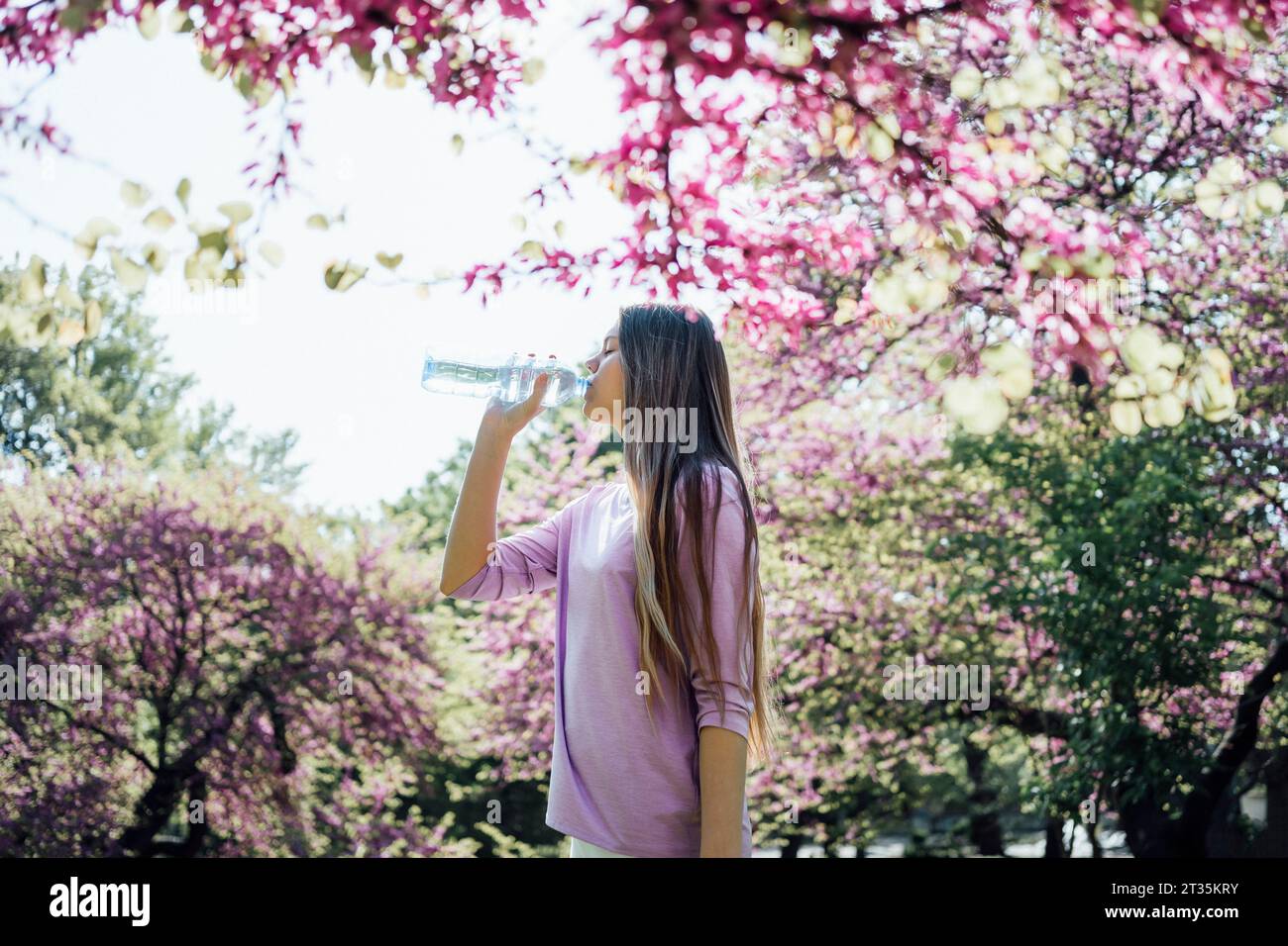 Adolescente buvant de l'eau au parc en fleurs Banque D'Images