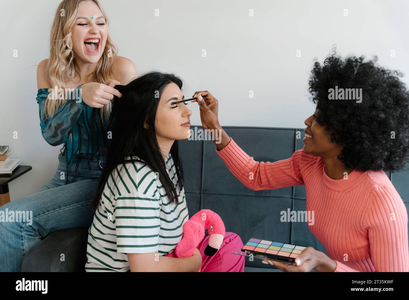 Ami aidant la femme à appliquer le maquillage et un autre ami tressant les cheveux Banque D'Images