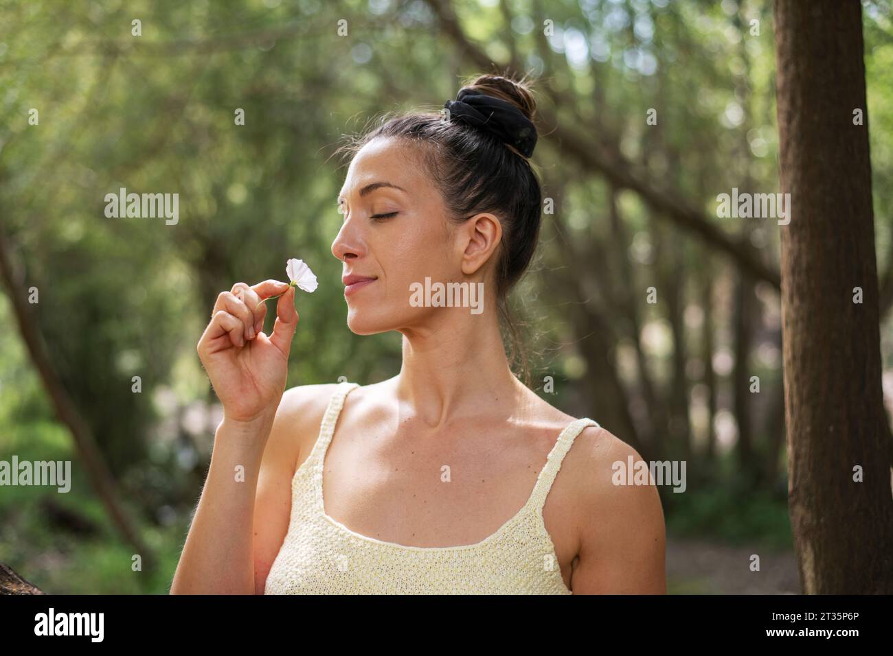 Femme avec un chignon de cheveux sentant la fleur dans la forêt Banque D'Images