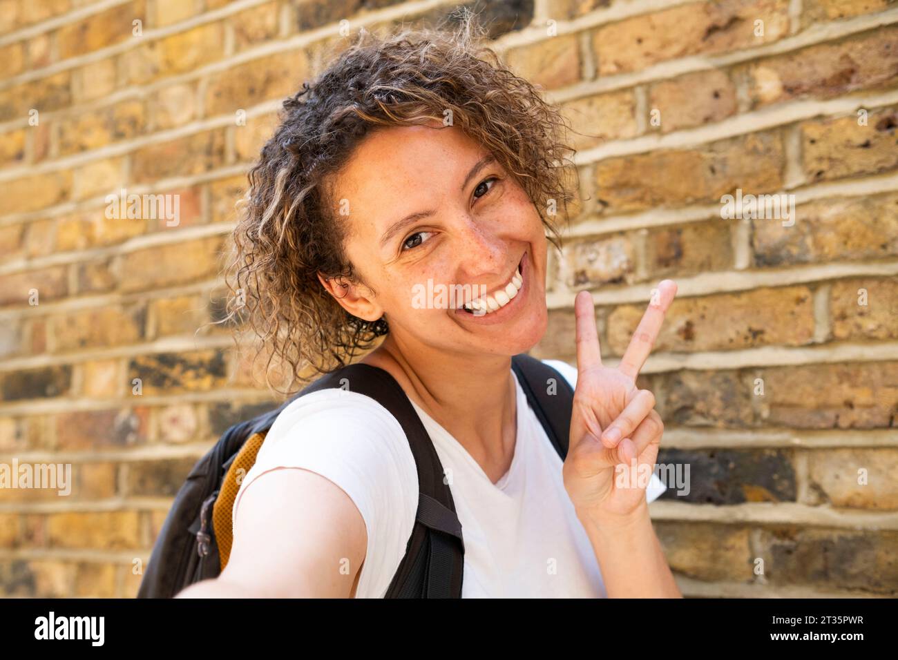Heureuse femme d'affaires faisant geste de paix devant le mur de briques Banque D'Images