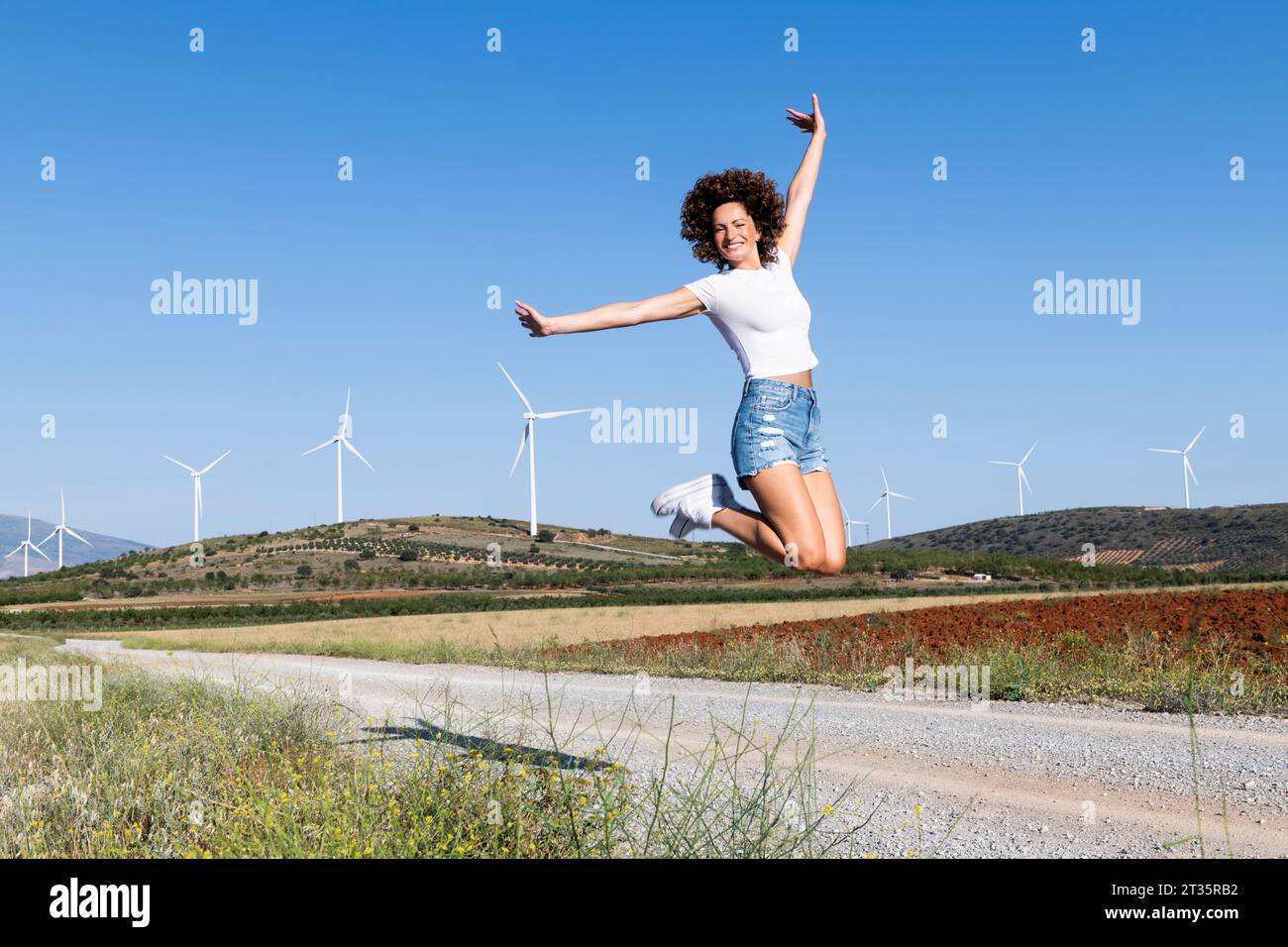 Femme joyeuse sautant devant les éoliennes Banque D'Images
