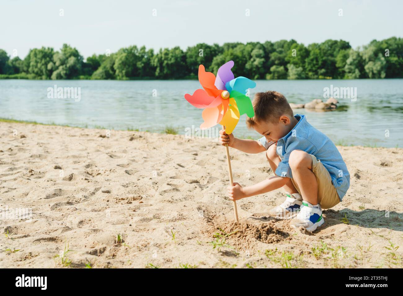 Garçon jouant avec jouet coloré de roue d'arc-en-ciel au bord du lac Banque D'Images