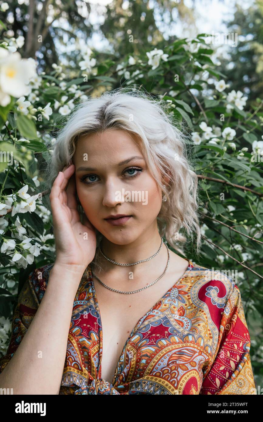 Belle femme touchant le visage et debout devant la plante de fleur Banque D'Images