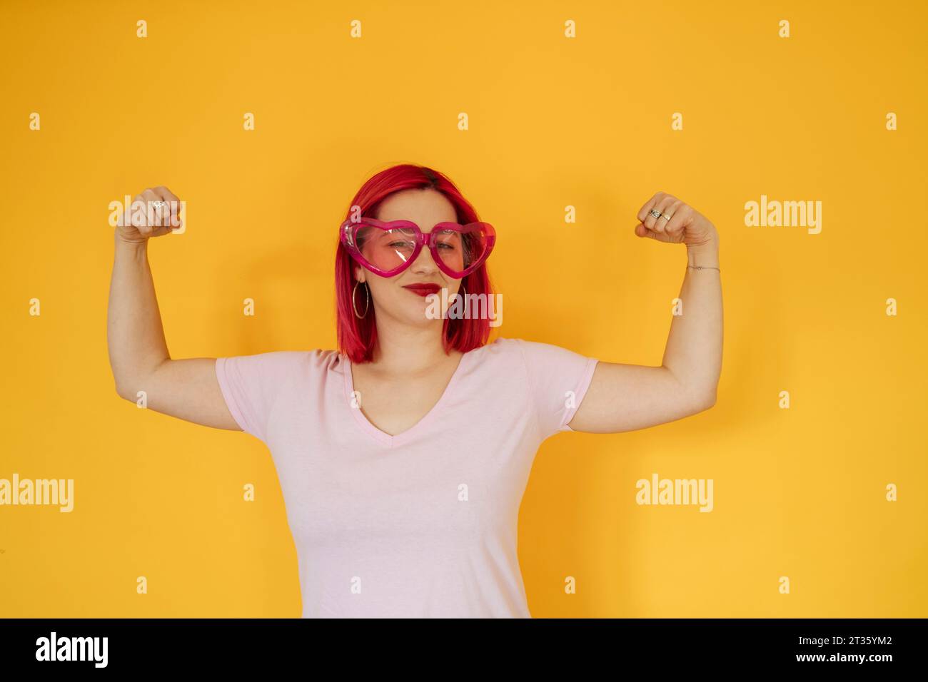 Femme souriante portant des lunettes de soleil en forme de coeur fléchissant les muscles Banque D'Images