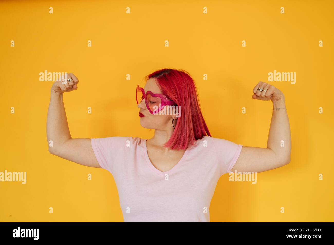 Femme portant des lunettes de soleil en forme de coeur fléchissant les muscles Banque D'Images