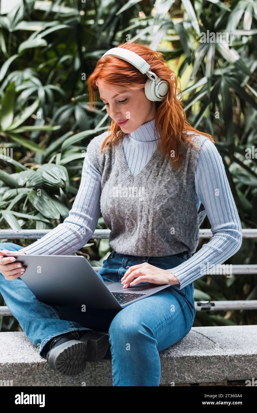 Femme d'affaires portant des écouteurs sans fil travaillant sur un ordinateur portable Banque D'Images