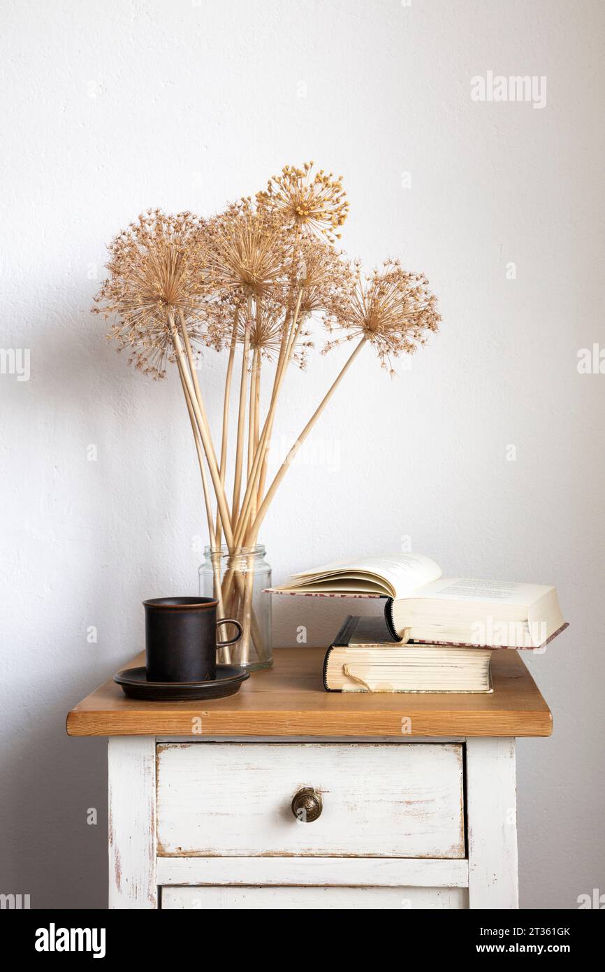 Livres, mug et fleurs Allium séchées sur petite armoire Banque D'Images