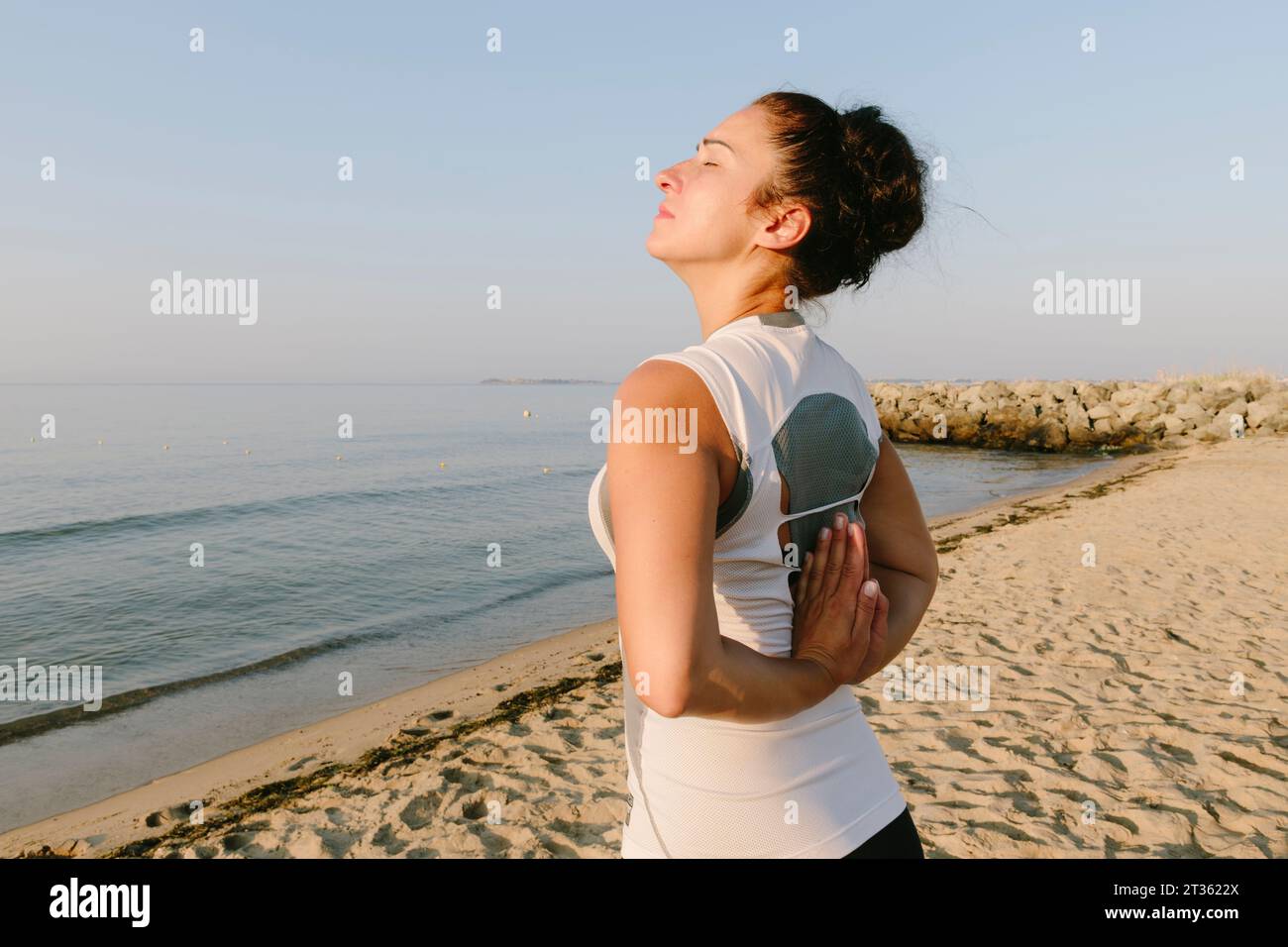 Femme avec les mains serrées derrière le dos pratiquant le yoga à la plage Banque D'Images