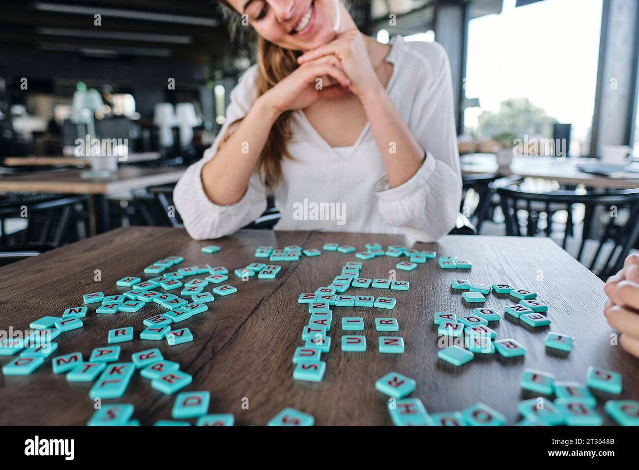 Jeune femme jouant au jeu de mots à la table de café Banque D'Images