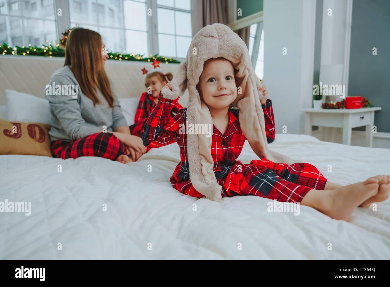 Garçon portant un chapeau d'animal assis sur le lit avec la famille à la maison Banque D'Images