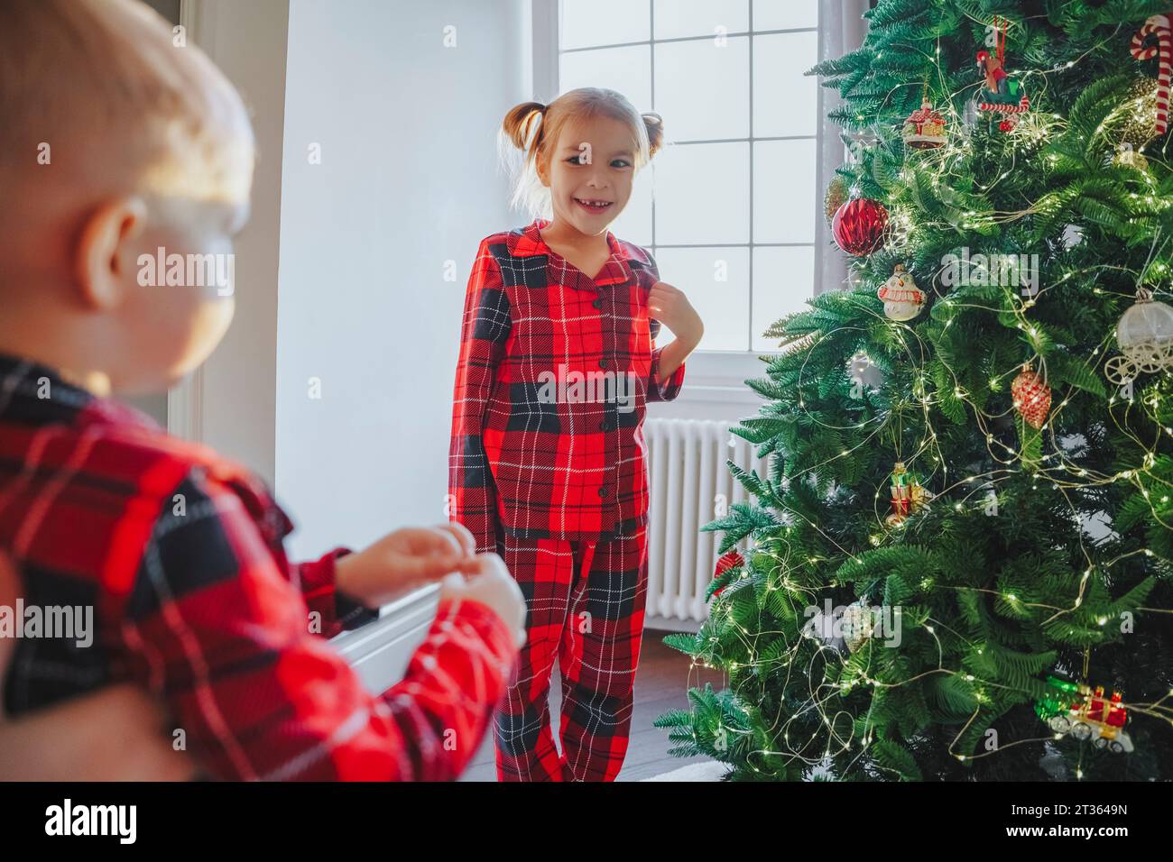 Sœur souriante regardant frère près de l'arbre de Noël à la maison Banque D'Images