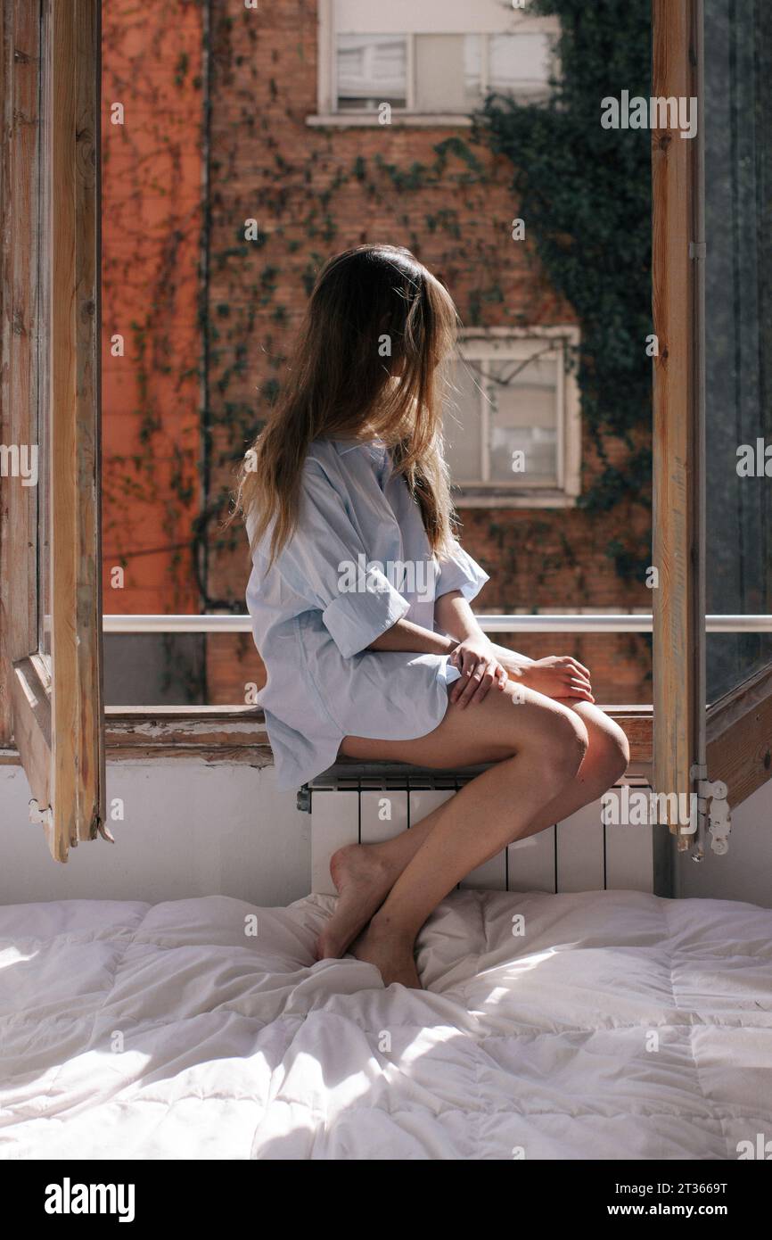 Femme assise et regardant par la fenêtre à la maison Banque D'Images