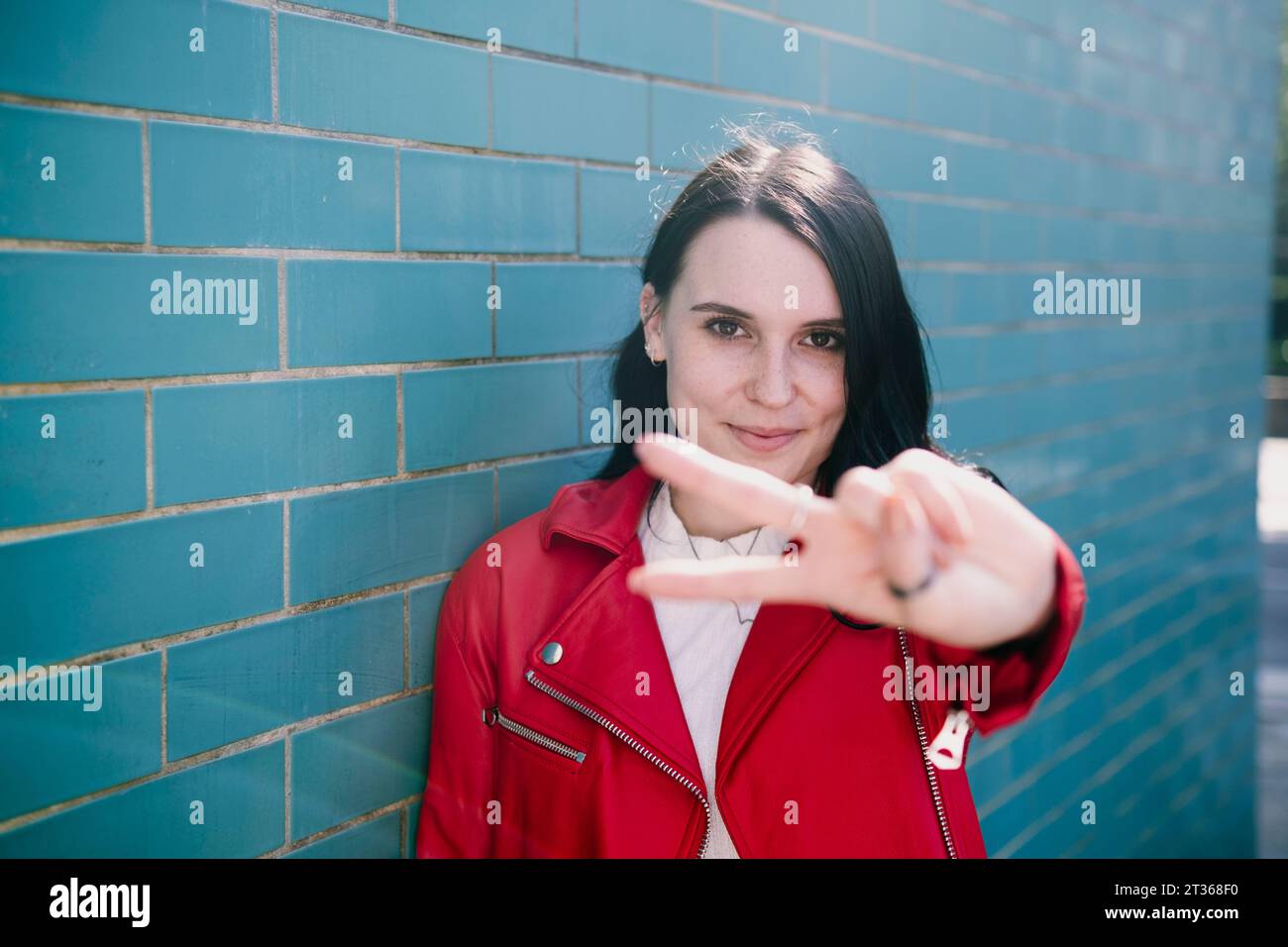 Jeune femme souriante montrant un geste de signe de paix devant le mur de briques Banque D'Images