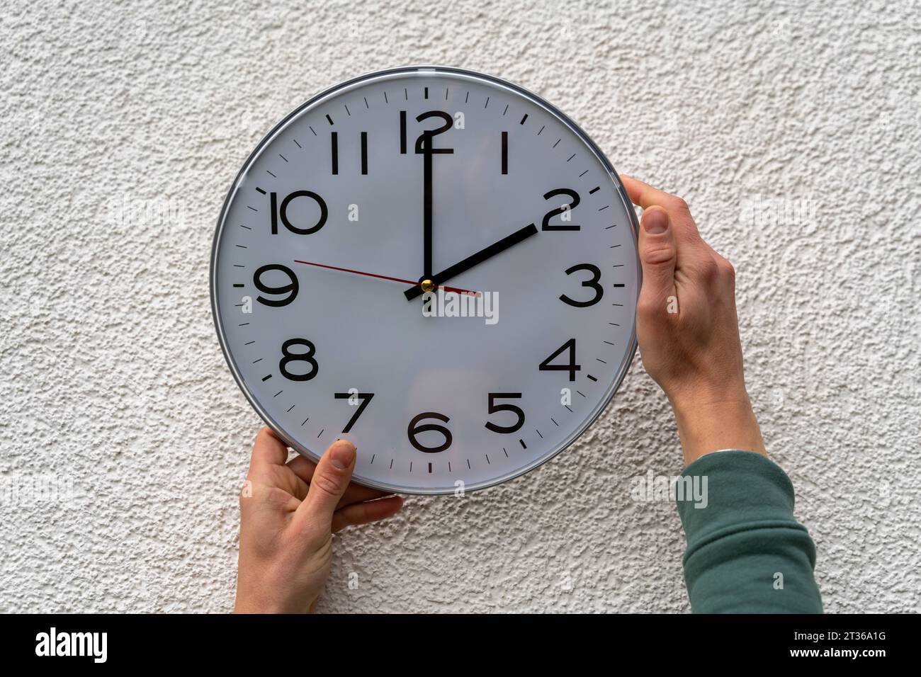 Augsbourg, Bavière, Allemagne - 17 octobre 2023 : l'homme fixe une horloge accrochée au mur à l'heure d'hiver. Concept de changement de temps *** Mann stellt eine an der Wand hängende Uhr UM auf Winterzeit. Zeitumstellung Konzept Banque D'Images