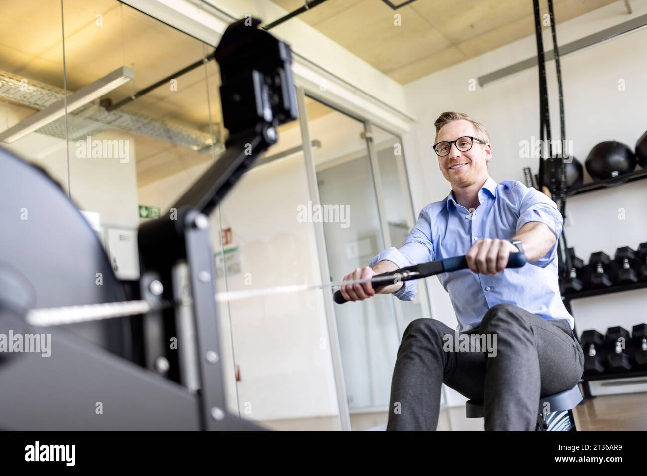 Homme d'affaires souriant exerçant avec de l'équipement dans la salle de gym de bureau Banque D'Images
