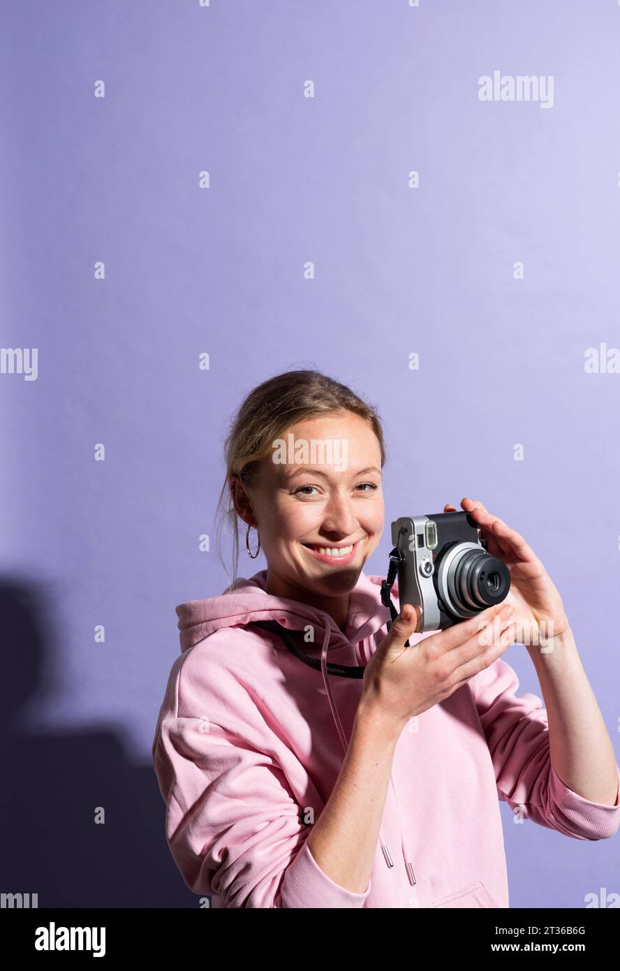 Femme souriante tenant la caméra sur fond violet Banque D'Images