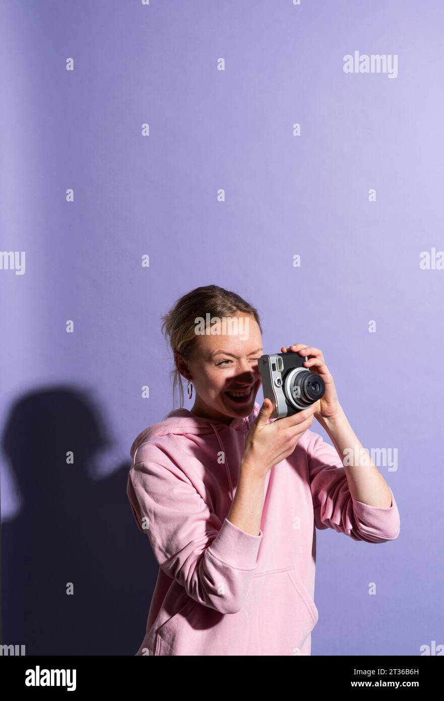 Femme souriante photographiant à travers la caméra en studio Banque D'Images