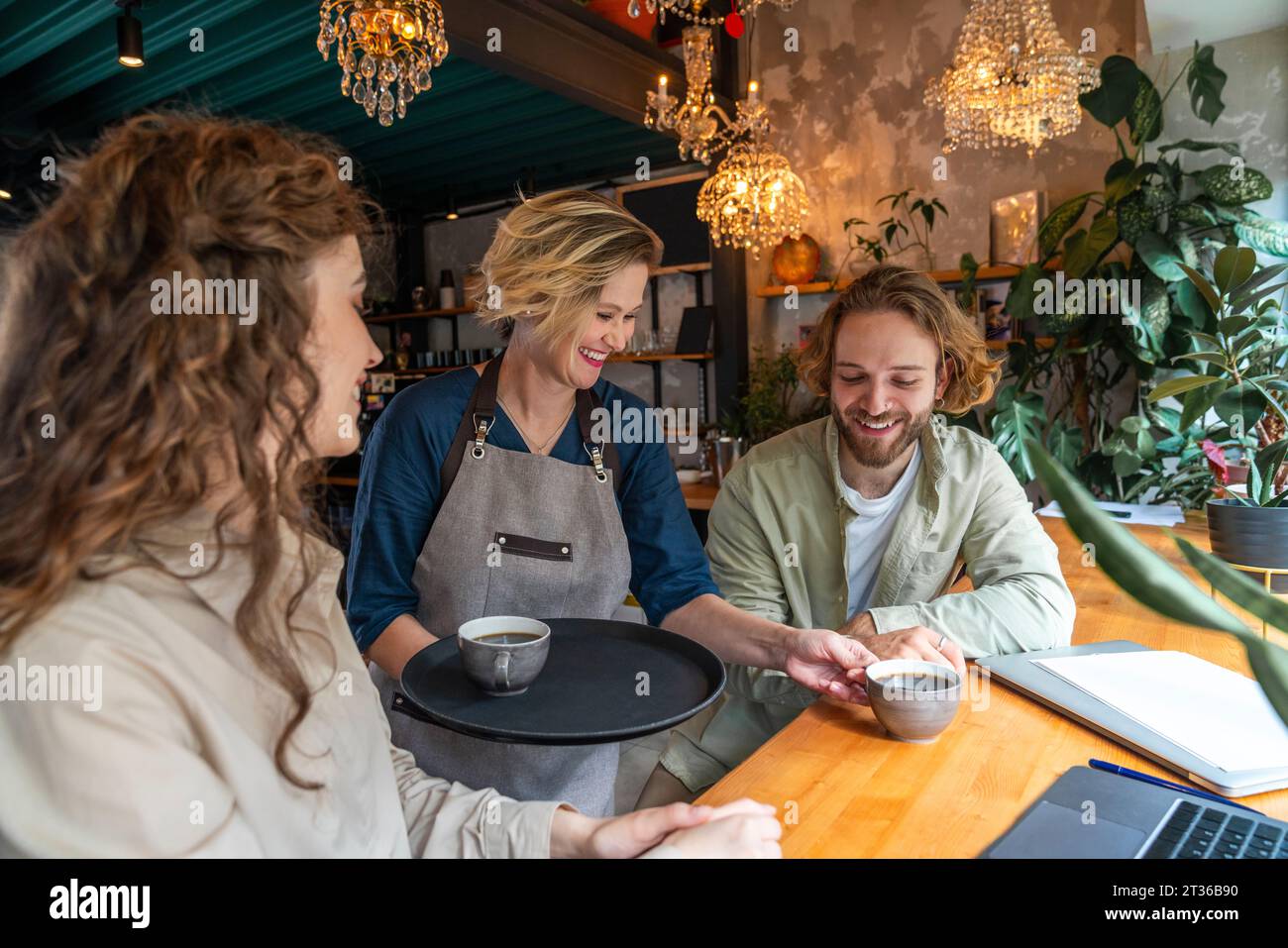 Serveuse souriante servant des cafés à des collègues d'affaires au café Banque D'Images