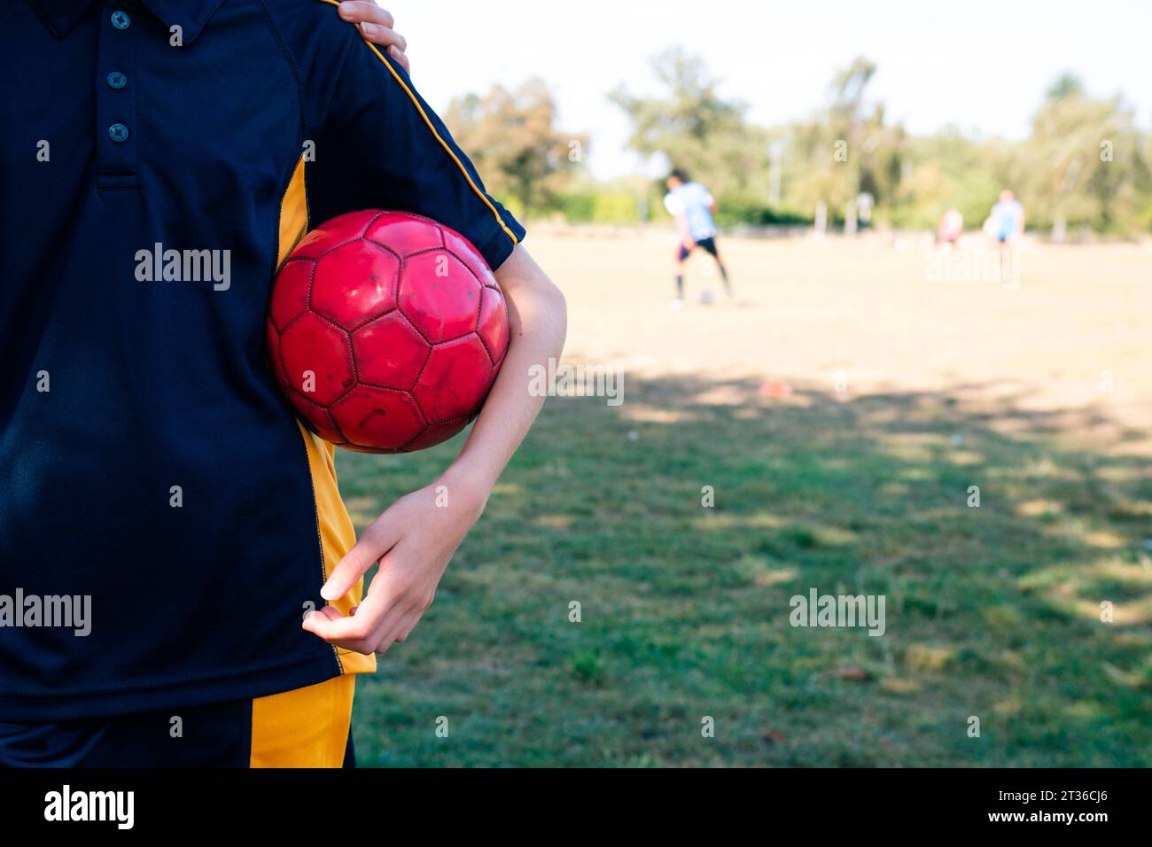 Fille tenant un ballon de football rouge sur un terrain de sport Banque D'Images