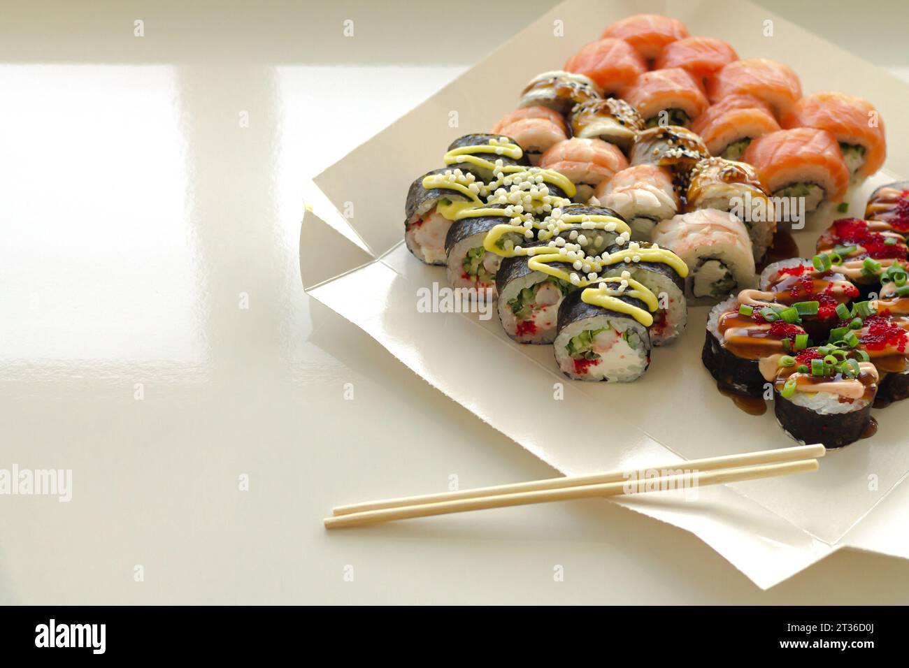 Rouleaux de sushi savoureux dans une boîte de papier jetable sur une table blanche. Service de livraison Japan Food dans le concept de conteneur écologique Banque D'Images