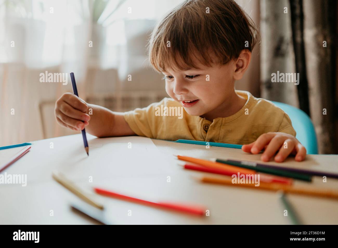 Dessin de garçon souriant avec un crayon de couleur à la maison Banque D'Images