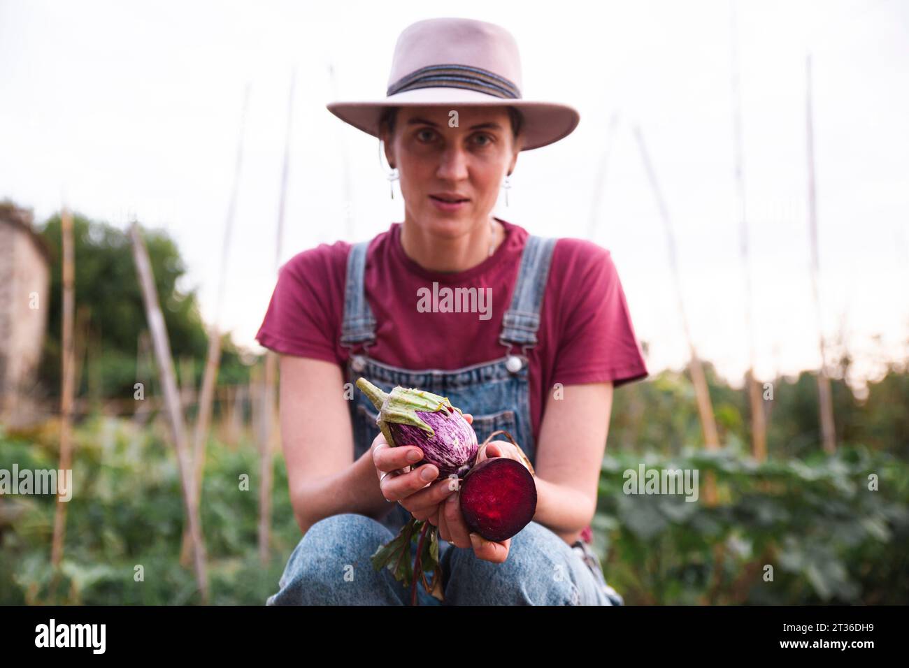 Femme portant un chapeau tenant l'aubergine et la betterave commune dans le verger Banque D'Images