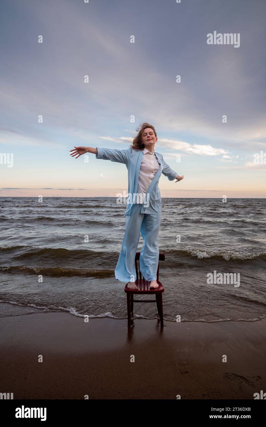 Femme debout avec les bras tendus sur une chaise à la plage Banque D'Images