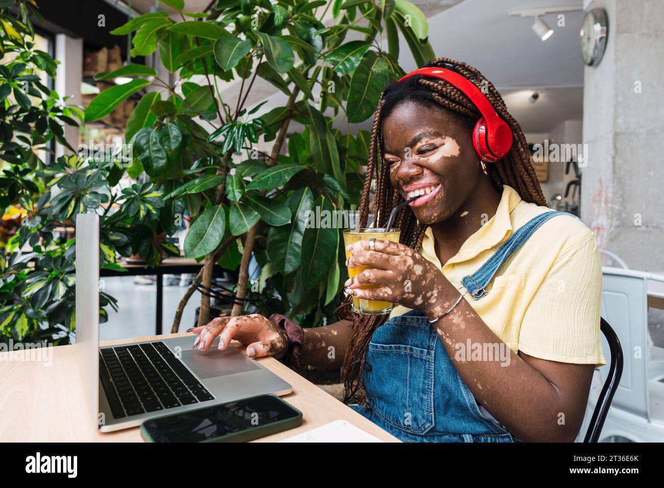 Heureux jeune freelance travaillant sur ordinateur portable et buvant du jus dans le café Banque D'Images