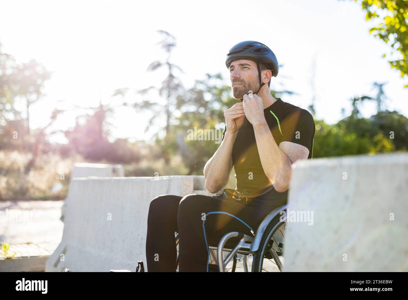 Athlète mature fixant le casque de sport assis sur un fauteuil roulant Banque D'Images