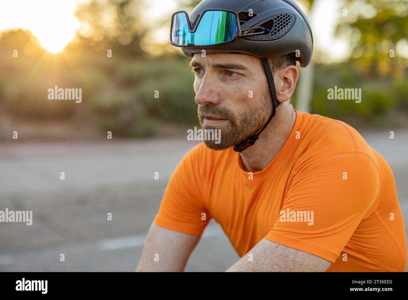 Homme contemplatif avec casque de sport et lunettes de soleil au coucher du soleil Banque D'Images