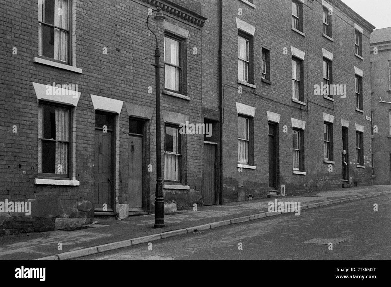 Dame regardant de sa porte dans une rue de maisons mitoyennes victoriennes, pendant le nettoyage des bidonvilles et la démolition de St ann's Nottingham, 1969-1972 Banque D'Images